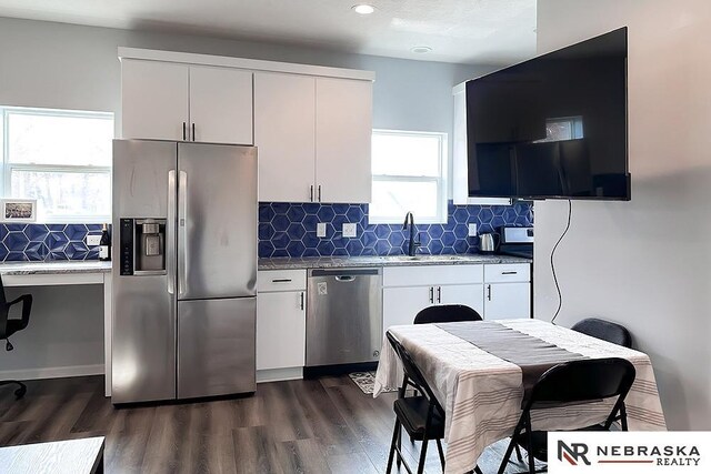 kitchen with a sink, backsplash, stainless steel appliances, white cabinetry, and dark wood-style flooring