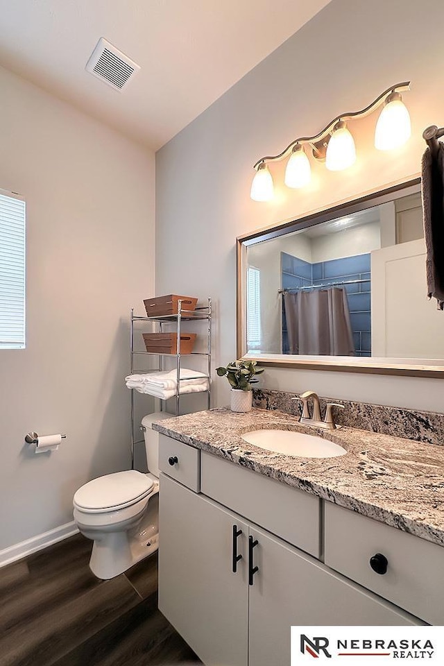 bathroom featuring vanity, wood finished floors, visible vents, baseboards, and toilet