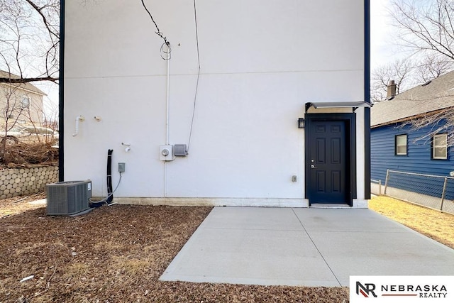 entrance to property featuring stucco siding, central AC, and fence