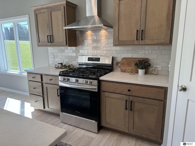 kitchen featuring decorative backsplash, gas range, light wood-style flooring, and wall chimney range hood