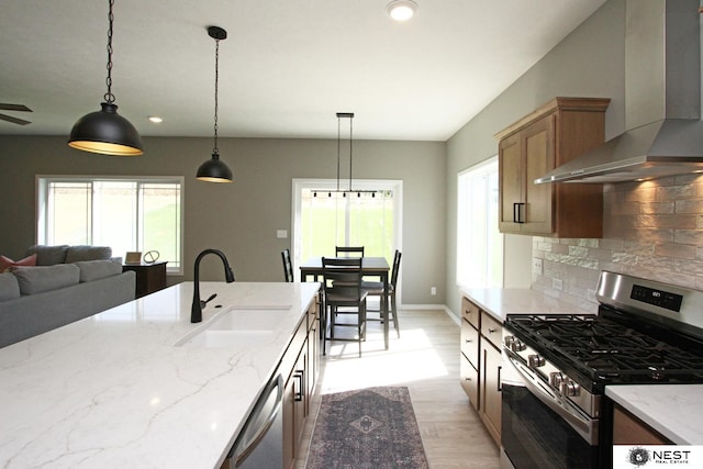 kitchen with a sink, wall chimney range hood, tasteful backsplash, appliances with stainless steel finishes, and light wood finished floors