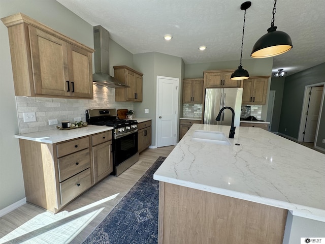 kitchen with a sink, a large island, appliances with stainless steel finishes, wall chimney range hood, and decorative light fixtures