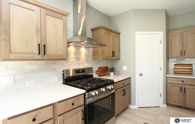 kitchen with stainless steel range with gas stovetop, light countertops, light wood-style floors, wall chimney exhaust hood, and tasteful backsplash