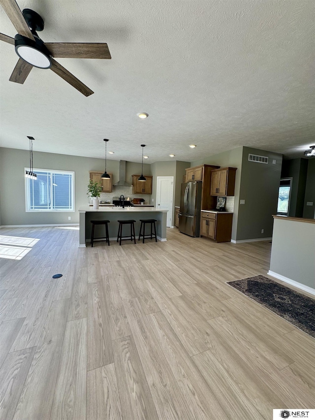 unfurnished living room with a sink, visible vents, baseboards, and light wood-style floors