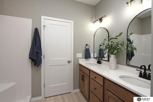 bathroom with double vanity, wood finished floors, baseboards, and a sink