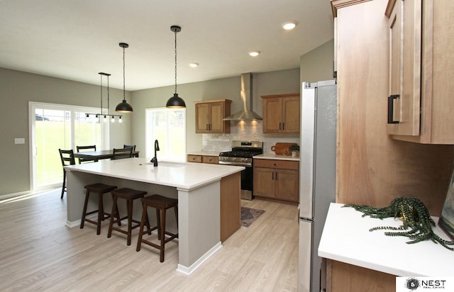 kitchen featuring light wood finished floors, a kitchen bar, decorative backsplash, stainless steel appliances, and wall chimney exhaust hood