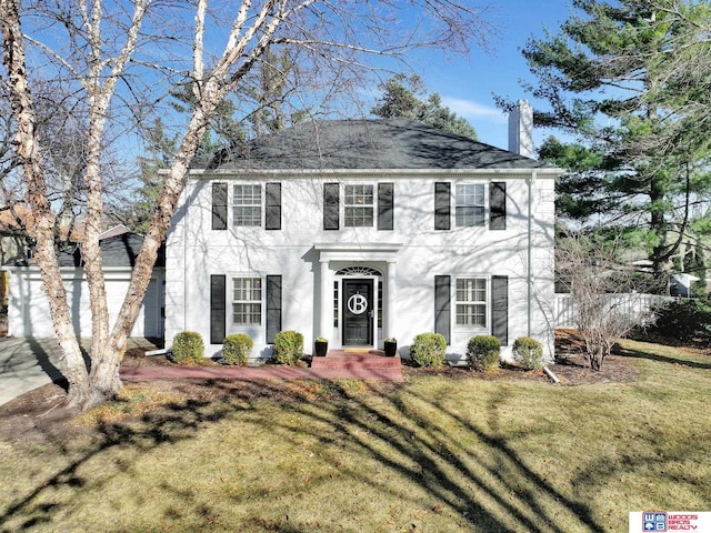 colonial home with a front lawn, an attached garage, and driveway