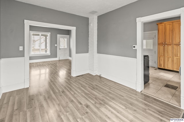 spare room featuring a wainscoted wall, light wood-style floors, visible vents, and ornate columns