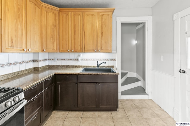 kitchen with dark stone counters, decorative backsplash, light tile patterned flooring, gas stove, and a sink