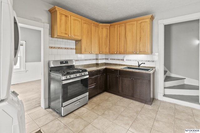 kitchen with gas stove, decorative backsplash, light tile patterned flooring, and a sink