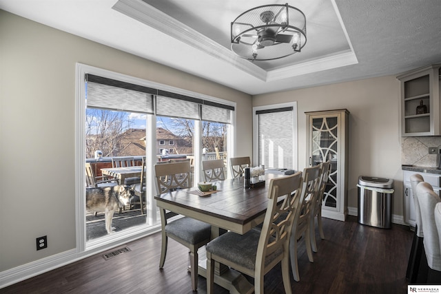 dining space with baseboards, visible vents, dark wood-style flooring, ornamental molding, and a raised ceiling