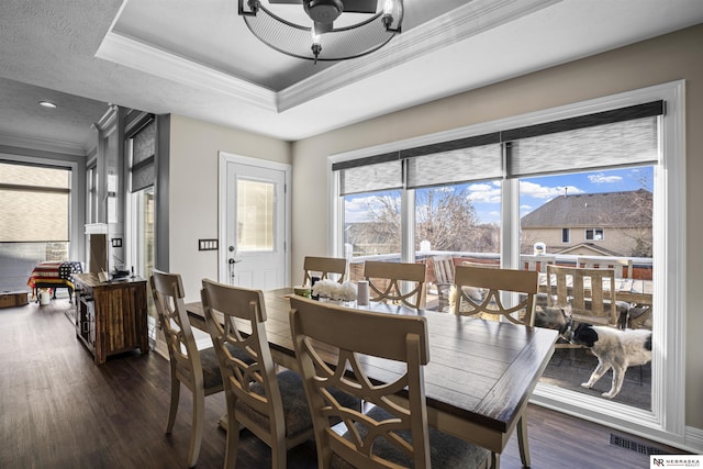 dining space with a tray ceiling, dark wood-type flooring, visible vents, and ornamental molding