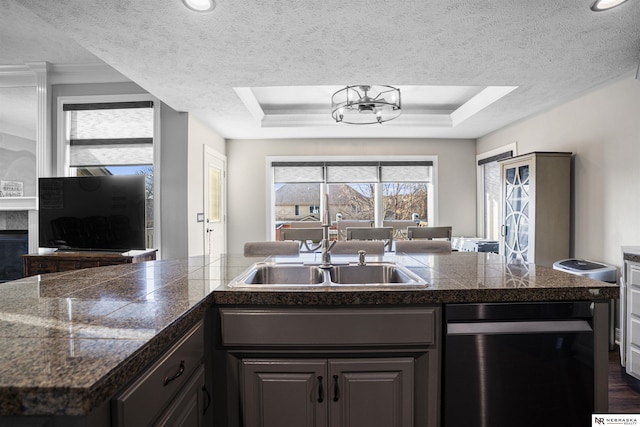 kitchen with a tray ceiling, a textured ceiling, dishwashing machine, and tile counters