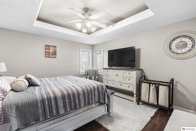 bedroom with a textured ceiling, a raised ceiling, baseboards, and wood finished floors