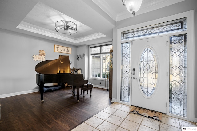 entrance foyer with crown molding, baseboards, a chandelier, light wood-type flooring, and a raised ceiling