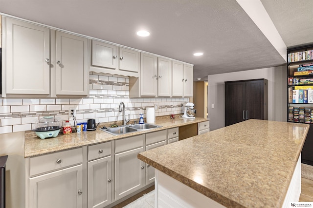 kitchen with tasteful backsplash, a kitchen island, light countertops, recessed lighting, and a sink