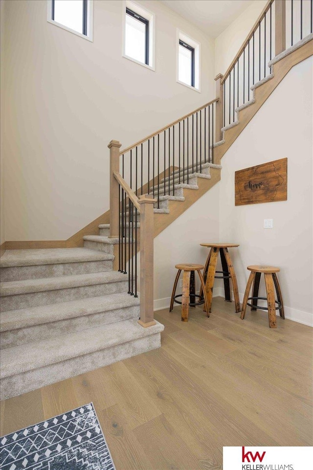 stairway featuring baseboards, a high ceiling, and wood finished floors