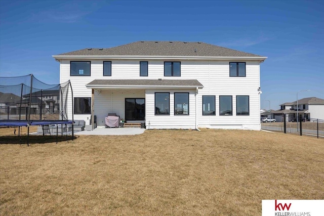 rear view of house with a trampoline, fence, a yard, roof with shingles, and a patio area