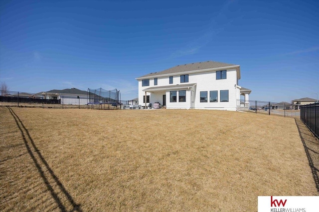 back of house with a trampoline, a lawn, and a fenced backyard