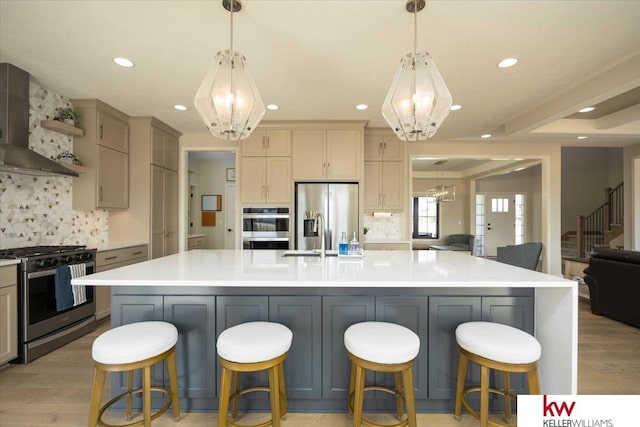 kitchen with light countertops, wall chimney range hood, appliances with stainless steel finishes, and a chandelier