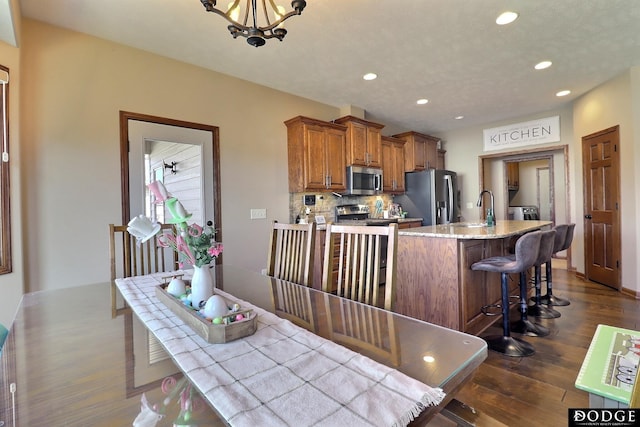 kitchen featuring a kitchen bar, dark wood-style floors, brown cabinetry, stainless steel appliances, and a sink