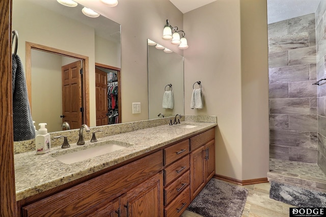 full bath with a sink, baseboards, double vanity, and a tile shower