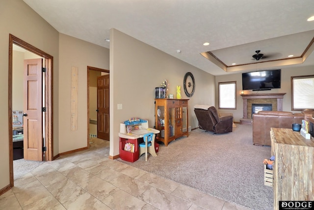 living room featuring a glass covered fireplace, light colored carpet, baseboards, and a tray ceiling