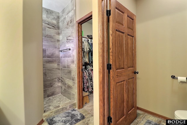 bathroom with a tile shower, a spacious closet, toilet, and baseboards