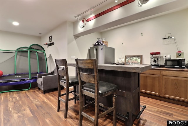 bar with black microwave, a bar, freestanding refrigerator, and light wood-style floors