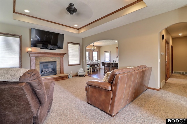 carpeted living room featuring visible vents, crown molding, baseboards, a tray ceiling, and arched walkways