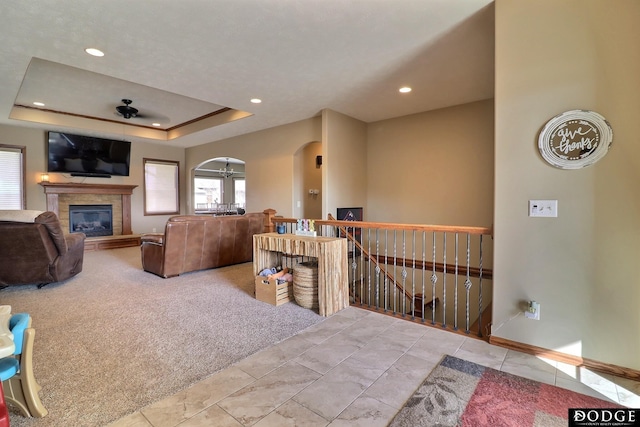 tiled living room featuring carpet floors, recessed lighting, a tile fireplace, arched walkways, and a raised ceiling