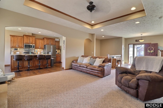 carpeted living area featuring a raised ceiling, crown molding, recessed lighting, and arched walkways