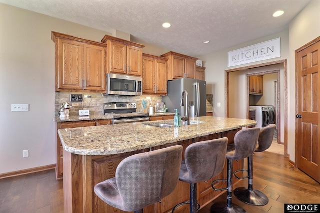 kitchen featuring tasteful backsplash, dark wood-type flooring, light stone countertops, appliances with stainless steel finishes, and independent washer and dryer