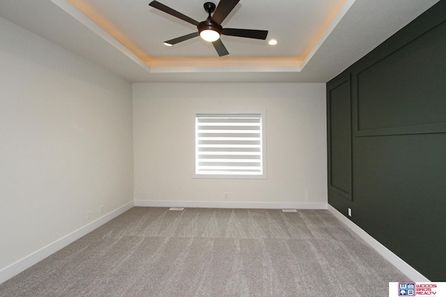 empty room featuring a tray ceiling, light colored carpet, baseboards, and ceiling fan