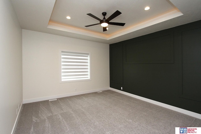 unfurnished room featuring a raised ceiling, light colored carpet, and baseboards