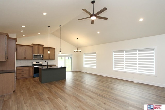 kitchen featuring dark countertops, backsplash, an island with sink, appliances with stainless steel finishes, and brown cabinetry