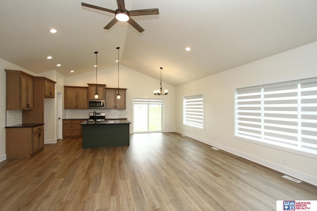 kitchen with a kitchen island with sink, tasteful backsplash, dark countertops, wood finished floors, and stainless steel appliances