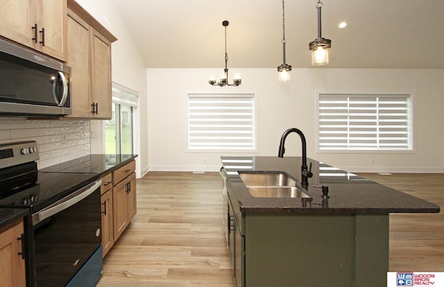 kitchen with light wood-type flooring, a kitchen island with sink, a sink, tasteful backsplash, and appliances with stainless steel finishes