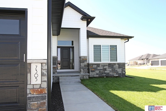 doorway to property featuring a yard, stone siding, and roof with shingles