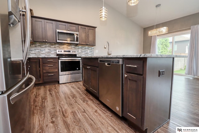 kitchen featuring wood finished floors, stainless steel appliances, dark brown cabinetry, vaulted ceiling, and backsplash