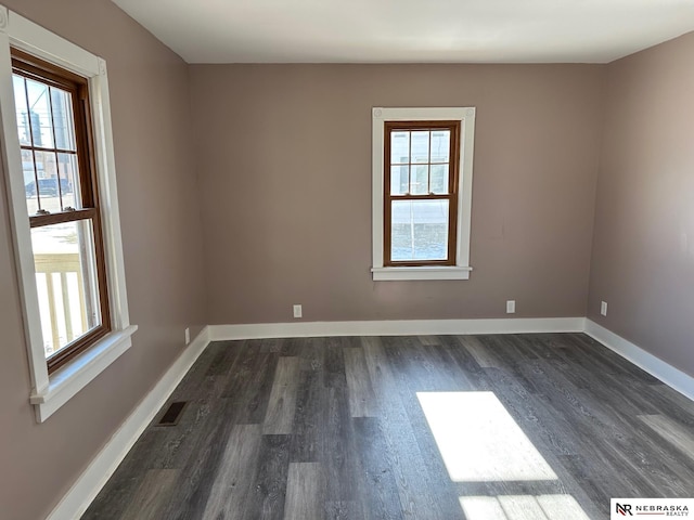 empty room featuring dark wood finished floors, visible vents, and baseboards