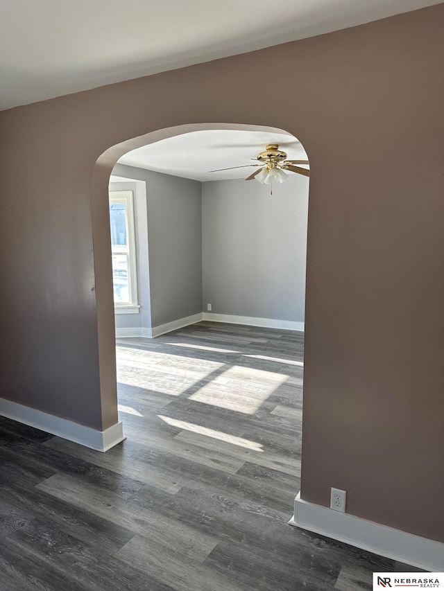 unfurnished room featuring baseboards, arched walkways, dark wood-type flooring, and a ceiling fan