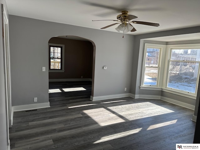 spare room featuring arched walkways, dark wood finished floors, baseboards, and ceiling fan