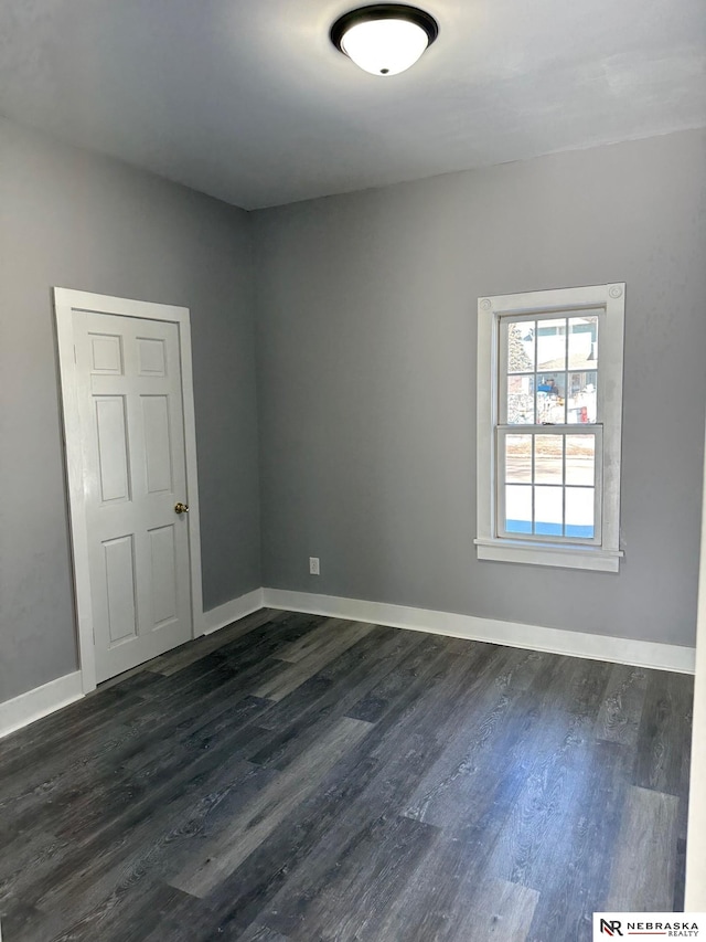 empty room featuring baseboards and dark wood-type flooring