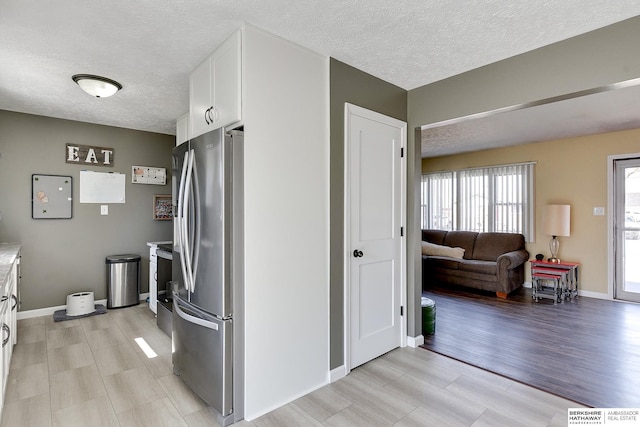 kitchen with light wood-type flooring, a textured ceiling, freestanding refrigerator, white cabinets, and light countertops