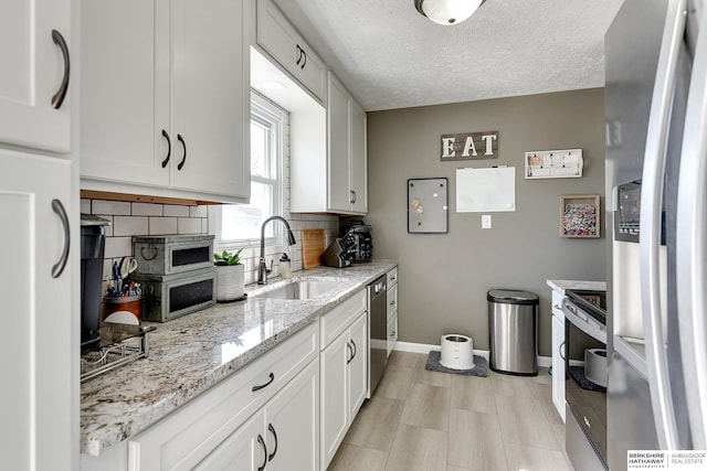 kitchen with a sink, a textured ceiling, appliances with stainless steel finishes, white cabinets, and decorative backsplash