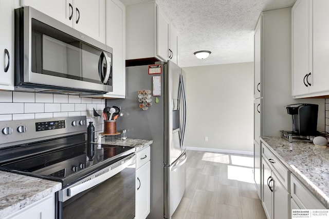 kitchen with a textured ceiling, backsplash, white cabinetry, stainless steel appliances, and baseboards