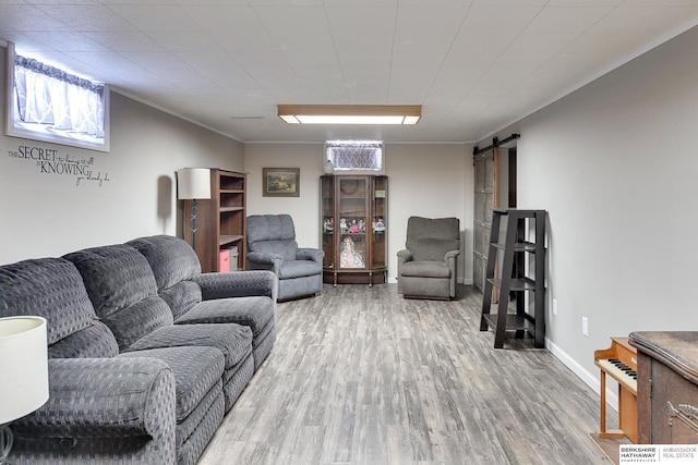 living area with a barn door, wood finished floors, baseboards, and ornamental molding