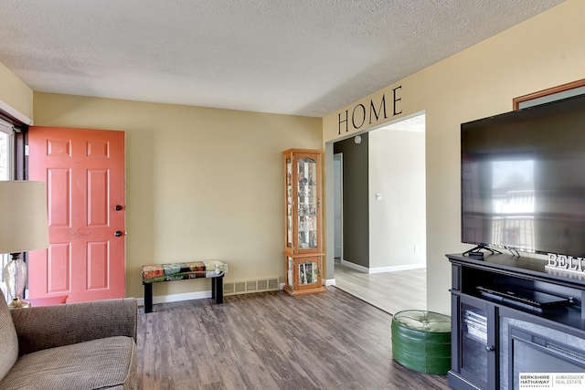 living room with baseboards, wood finished floors, visible vents, and a textured ceiling