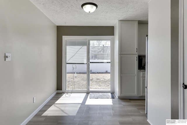 doorway with a textured ceiling, baseboards, and wood finished floors